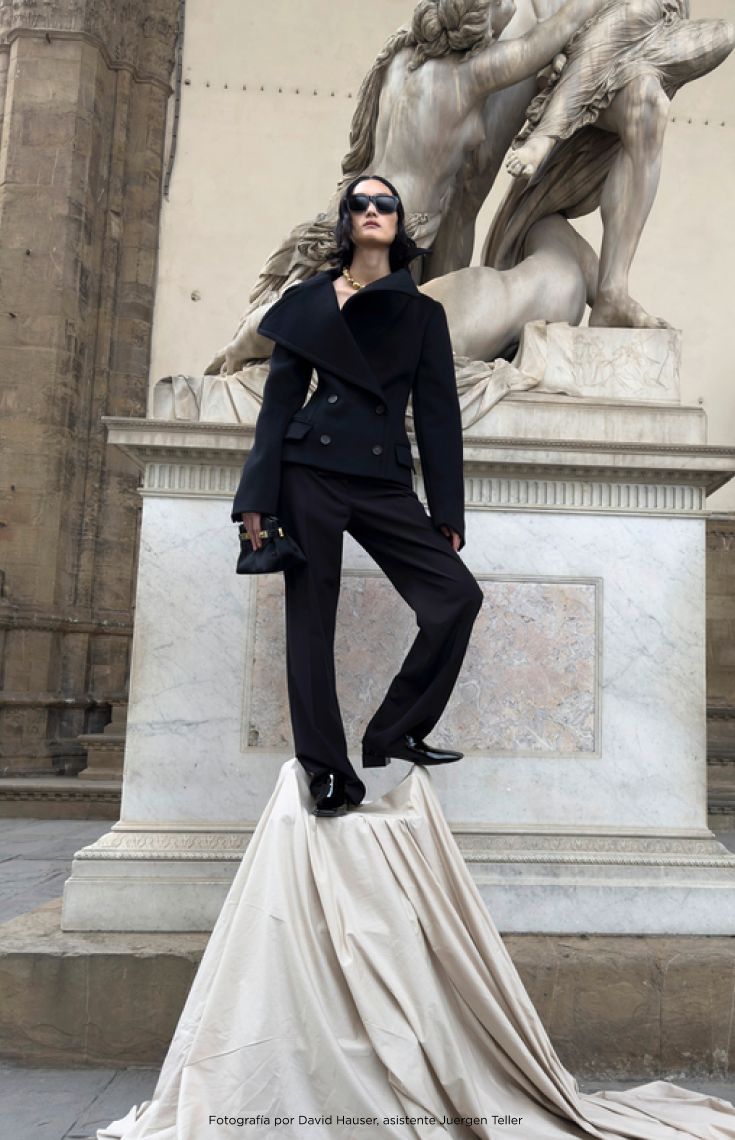 Mujer usando un conjunto de pantalon con abrigo color negro, de fondo una estatua grande de marmol