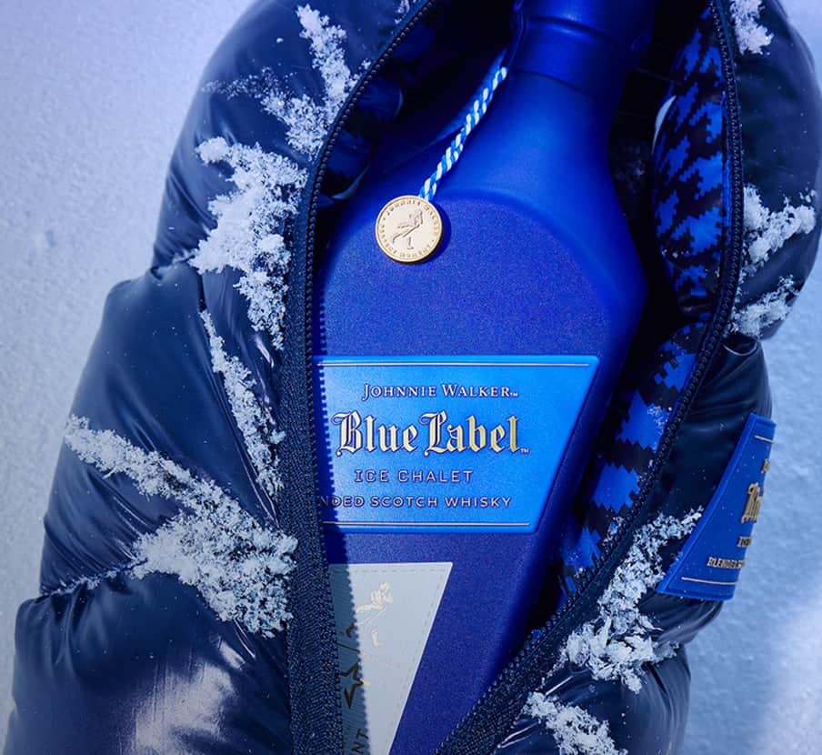 imagen de una botella de whisky BLUE LABER ICE CHALET tapada con una chamarra azul, de fondo hay nieve, JOHNNIE WALKER 