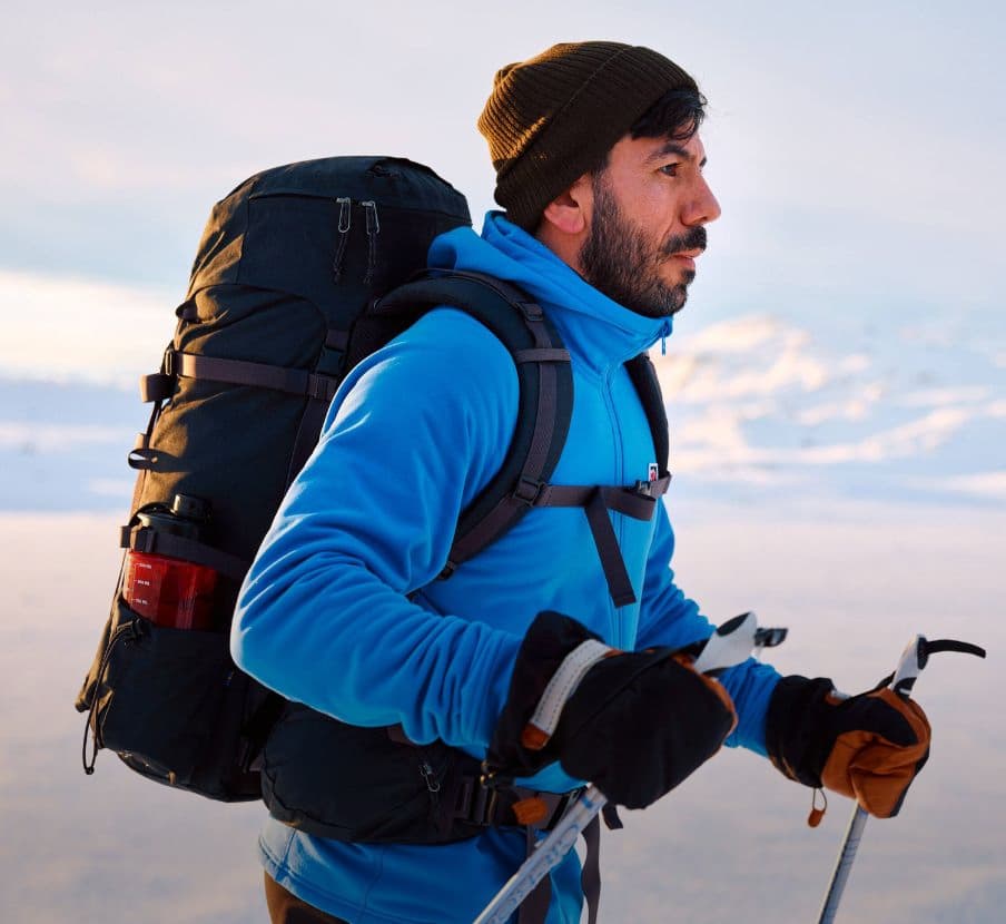 imagen de hombre en la vieve con chammarra azul, guantes, gorro y mochila negros, fjallraven