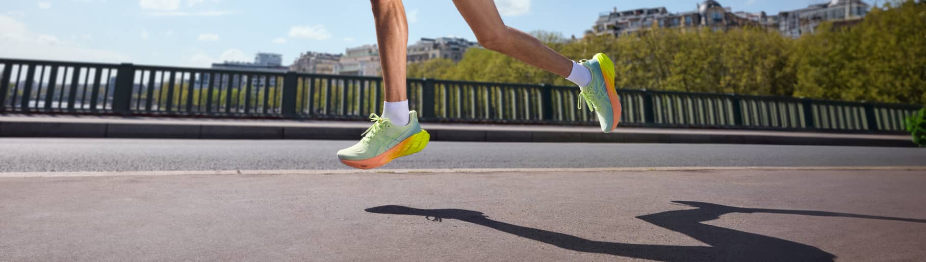 imagen de los pies de un hombre correindo, lleva unos tenis color verde claro con naranja de la marca ASICS