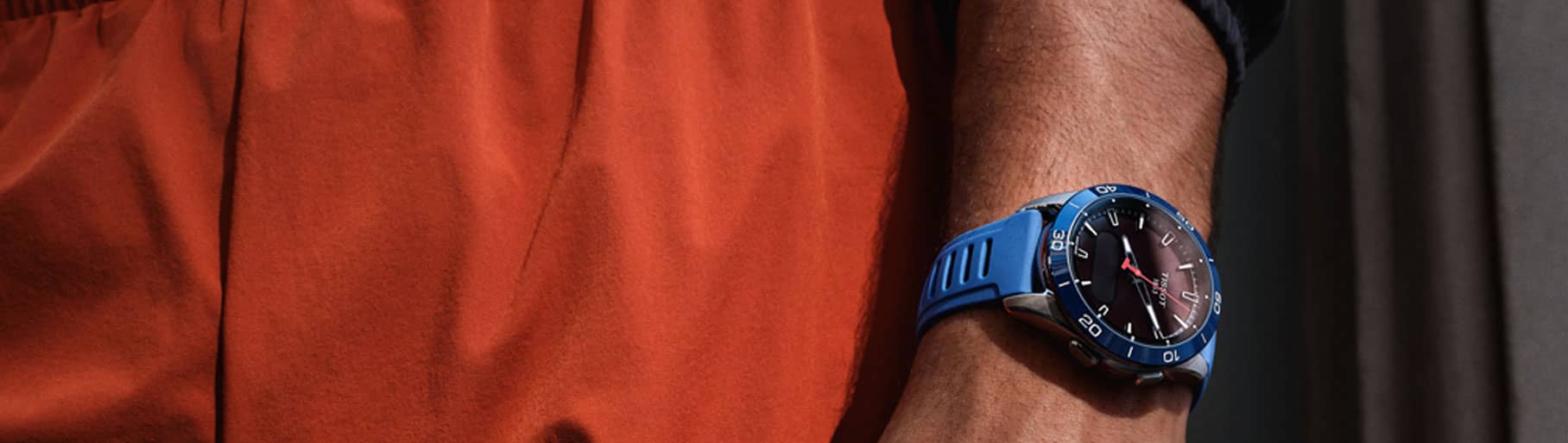 Imagen de hombre con playera naranja y reloj azul. TISSOT.