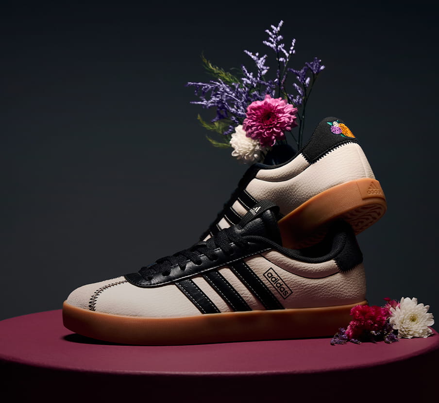 imagen de par de tenis negros con blanco con flores color blanco, morado y rosa dentro de la marca ADIDAS