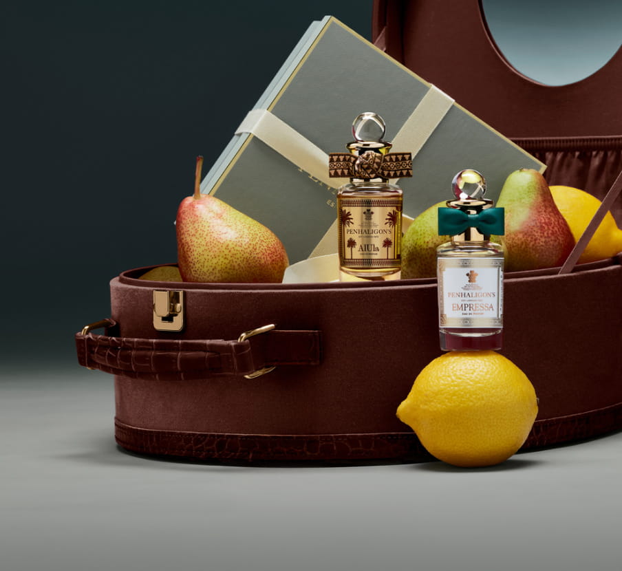 Imagen de dos lociones junto a un maletin con frutas PENHALIGON'S