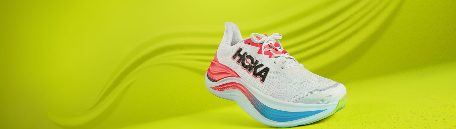 imagen un tenis color blanco con toques azul y rosa, y el nombre de la marca HOKA en letras negras