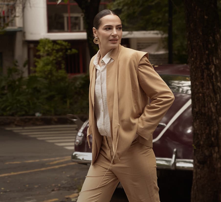 imagen de mujer caminando en la calle, usa blusa color blanca y conjunto de saco y pantalon de color beige. PERTEGAZ