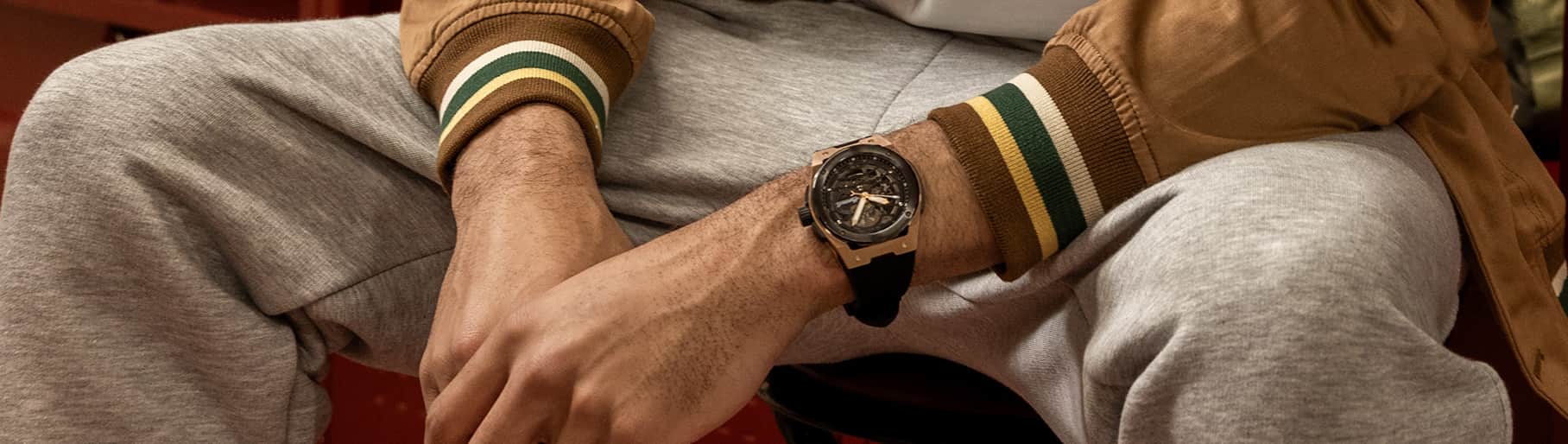 imagen de hombre con chamarra cafe, pants gris y  reloj dorado de la marca INGERSOLL 